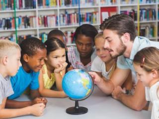 A diverse group of elementary students sitting around a globe with their teacher