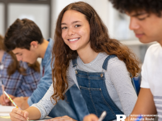 Row of middle school-aged students doing work with one looking at the camera and smiling